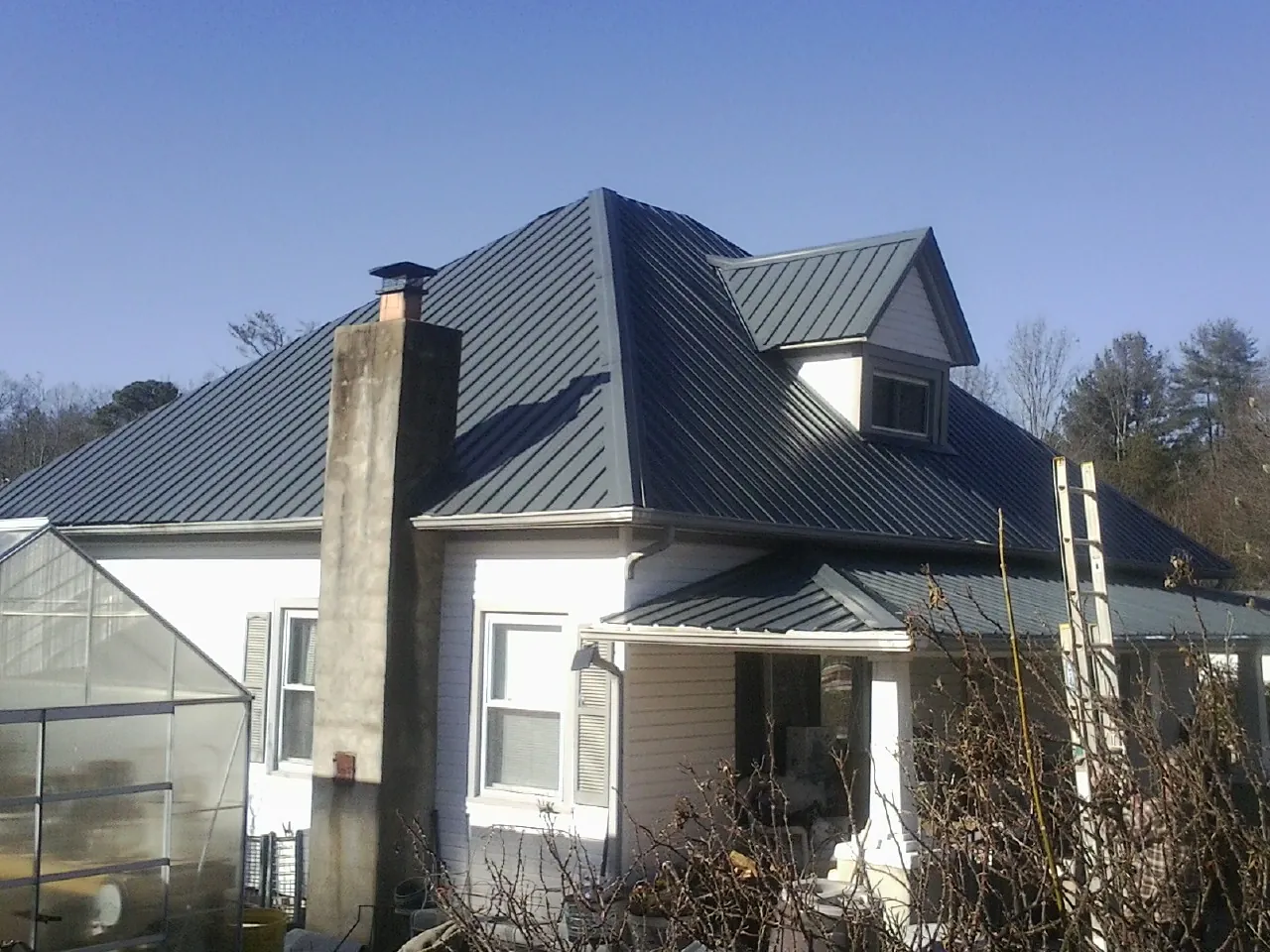 Dark blue standing seam metal roof on a white farmhouse with dormer — Slate & Tile Roof Repair by Roofing Brothers in Carbon