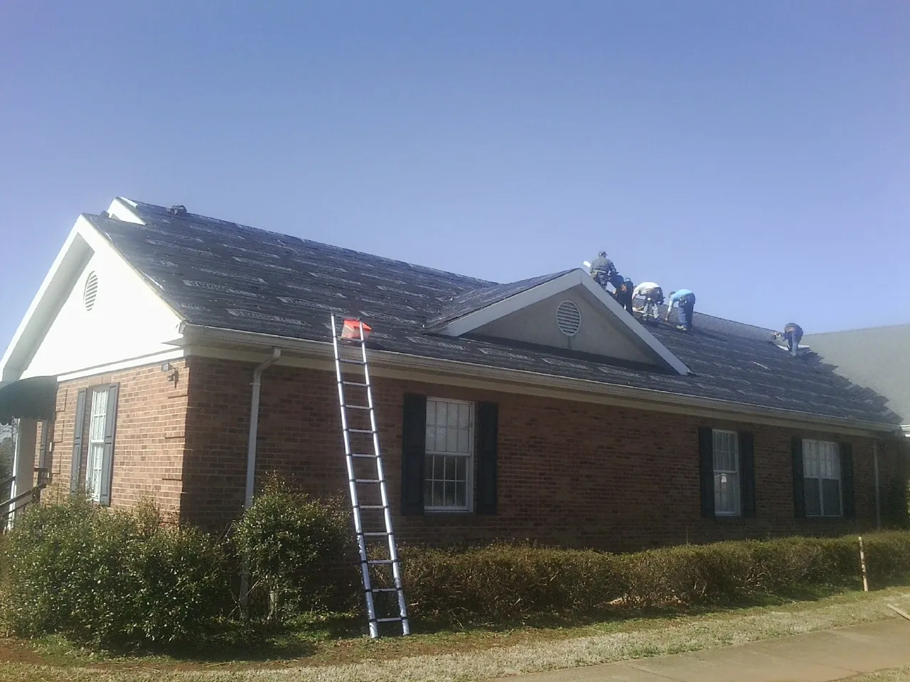 Crew tearing shingles off a brick ranch roof with a ladder set — Emergency Roof Repair work by our crew in Carbon