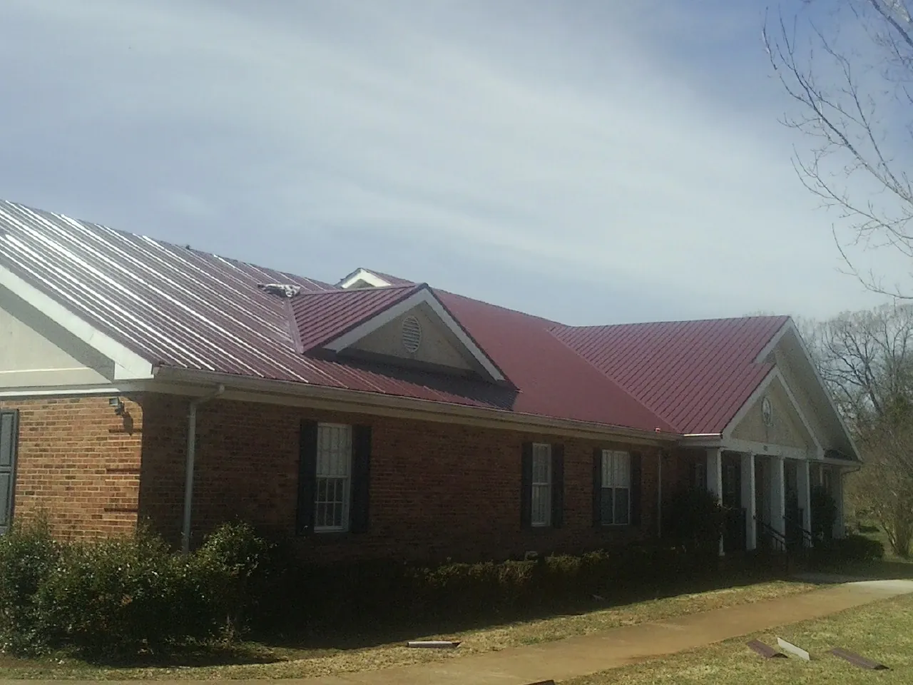 Red metal roof with gabled entries on a long brick building, from a Hail Damage Roof Repair job in Carbon