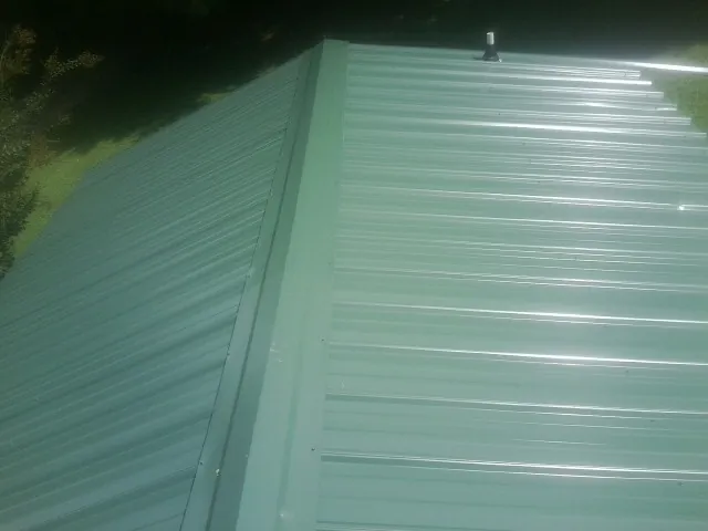 New green metal panels meeting at the ridge of a roof — Flat Roof Repair work by our crew in Carbon