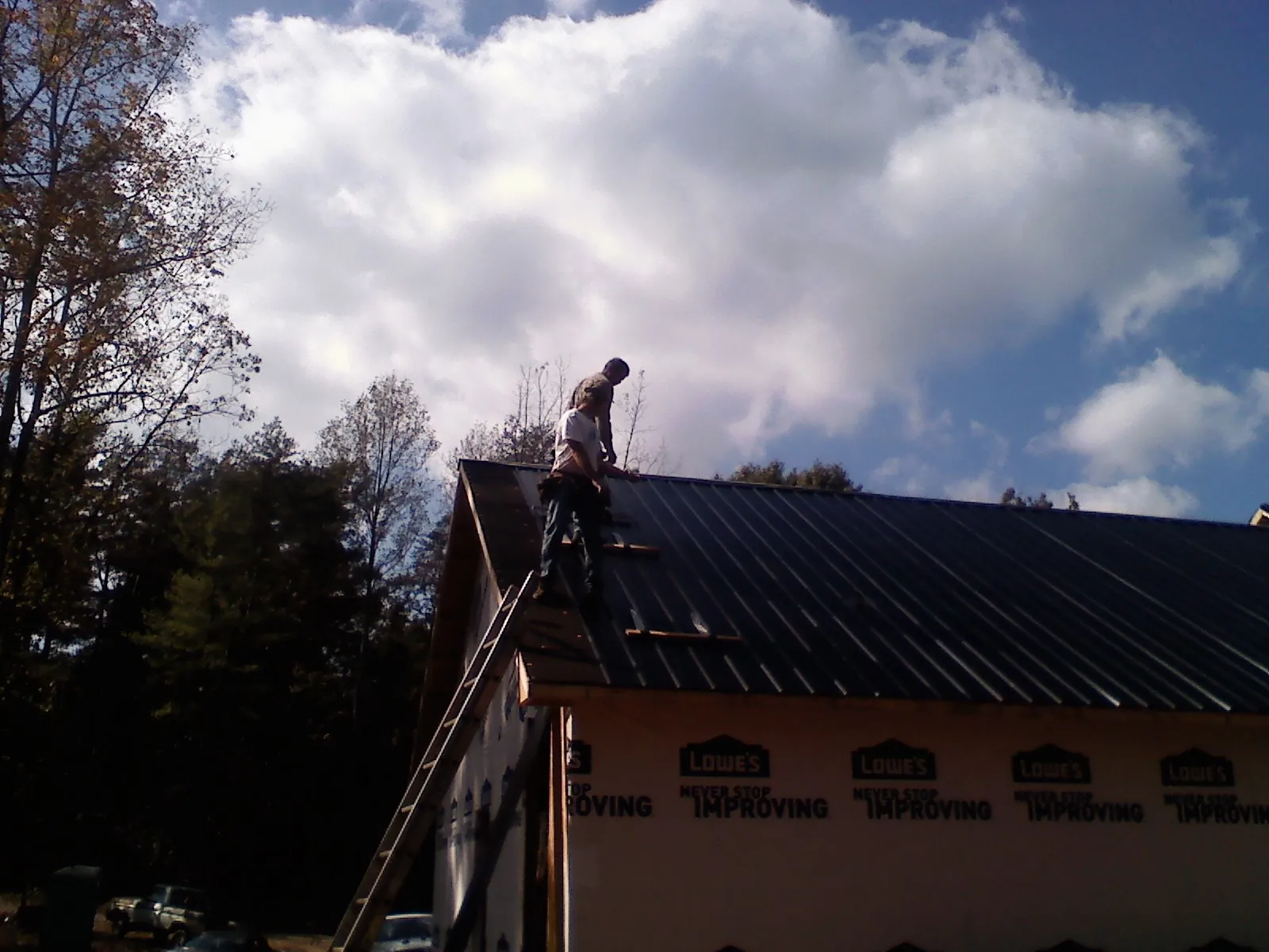 Roofer fastening dark metal panels high against a cloudy sky, from a Roof Inspection job in Carbon