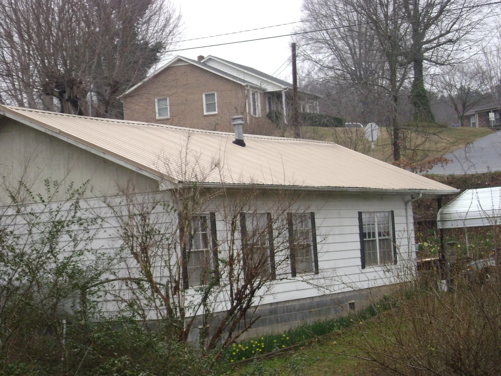 Tan metal roof on a white sided house set into a hillside — Commercial Roofing by Roofing Brothers in Carbon